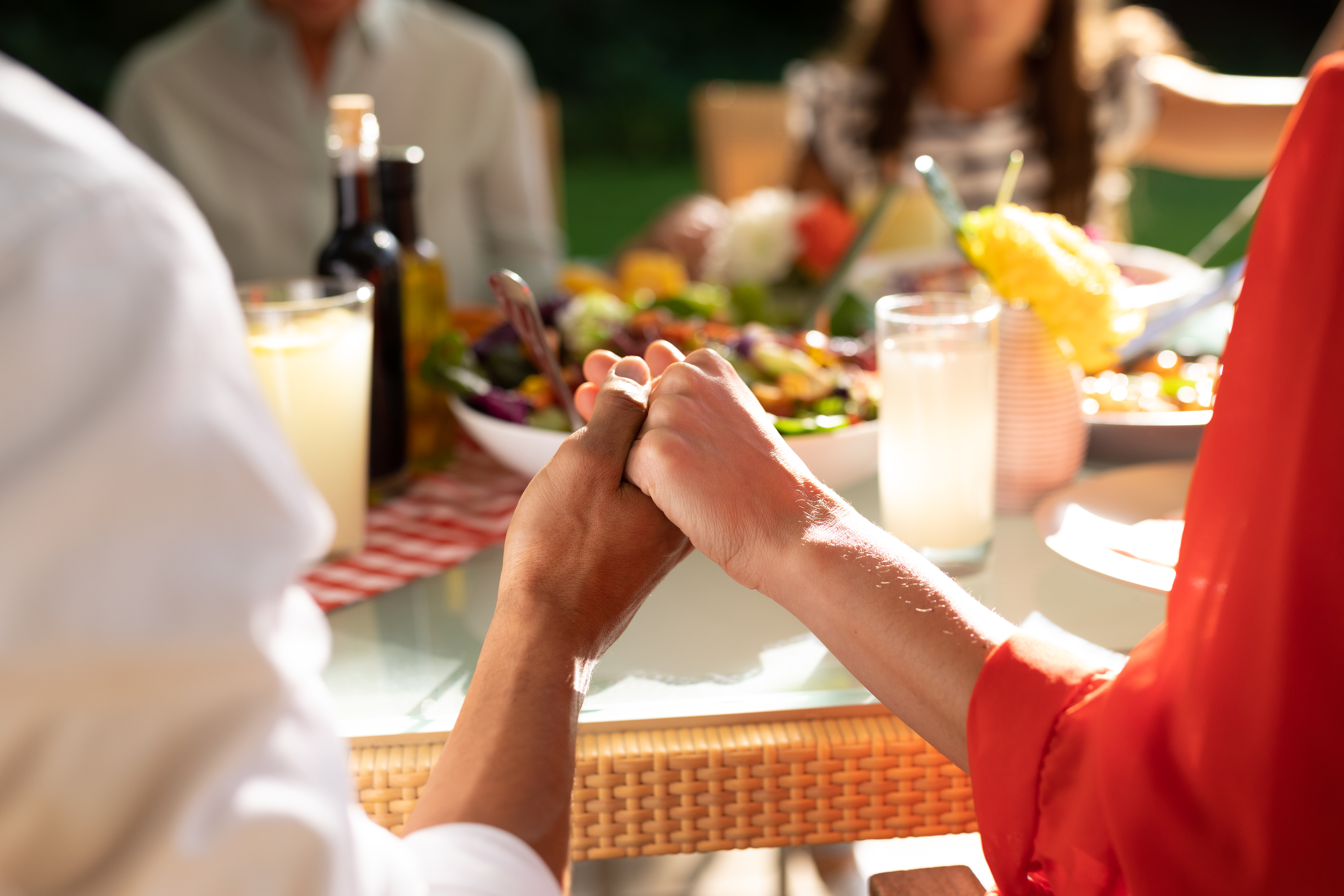 Rear view mid section of a Caucasian couple sitting outside with their family at a dinner table set for a meal, holding hands together in prayer. Family enjoying time at home, lifestyle concept